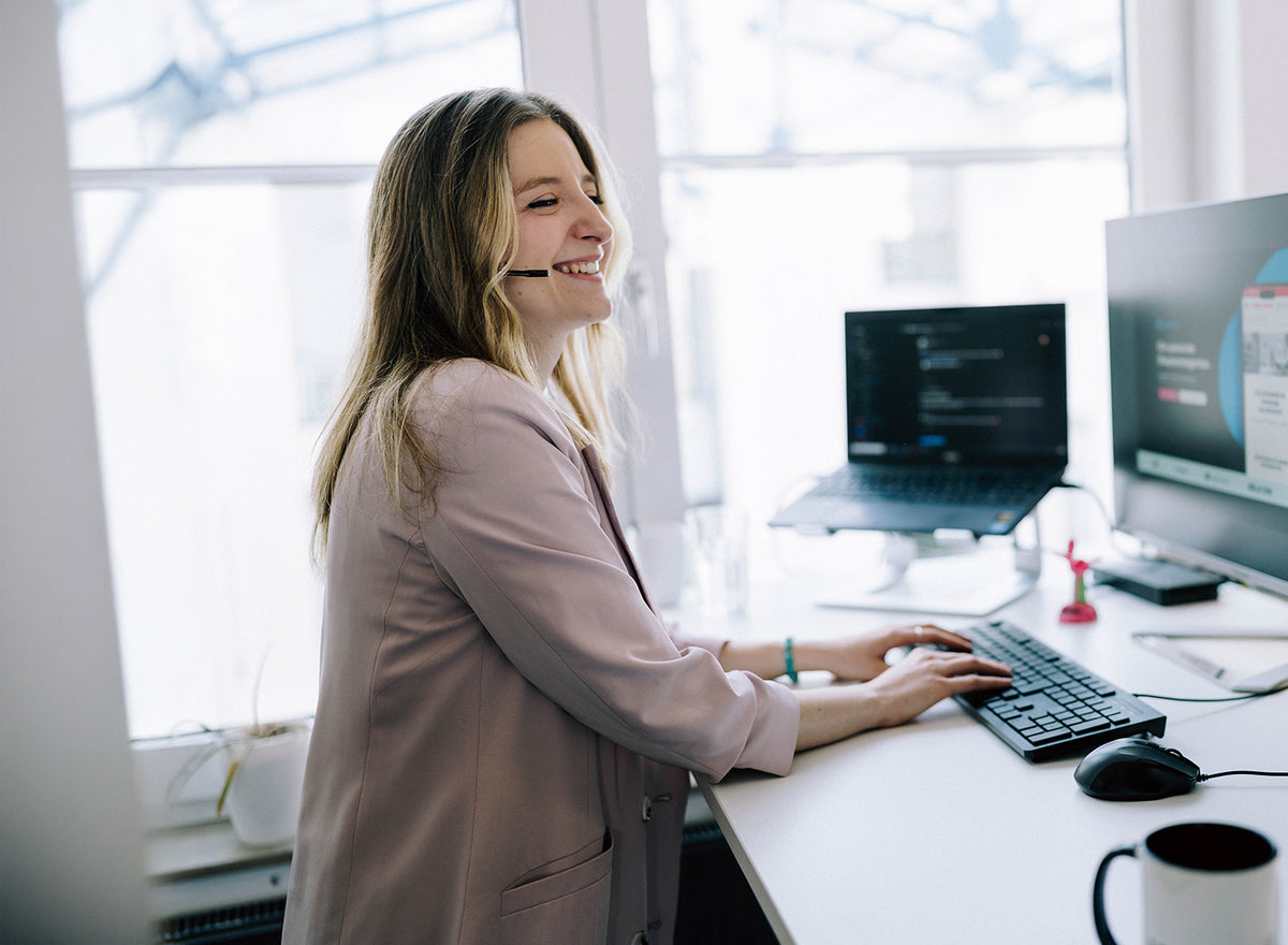 Online Marketing Managerin mit Headset an zwei Monitoren