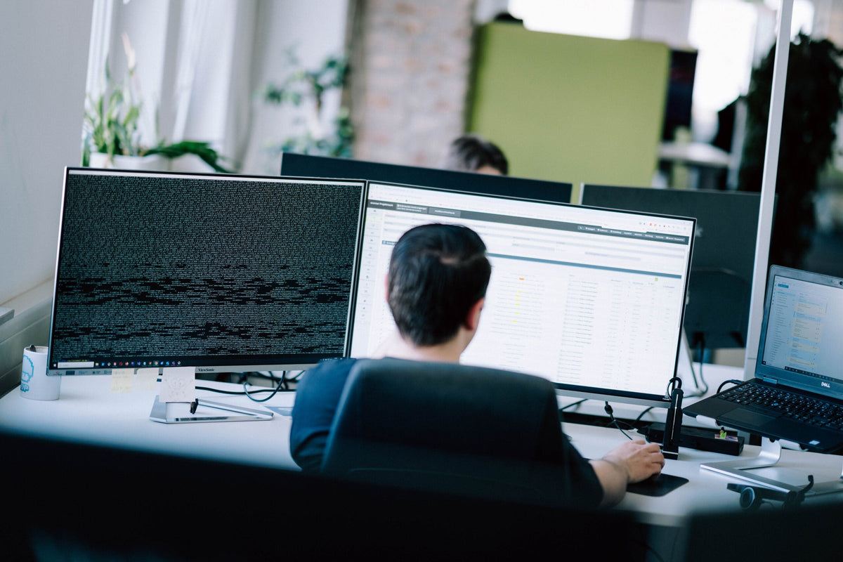 Entwickler arbeitet an mehreren Monitoren mit Code und Commerce System im Blick