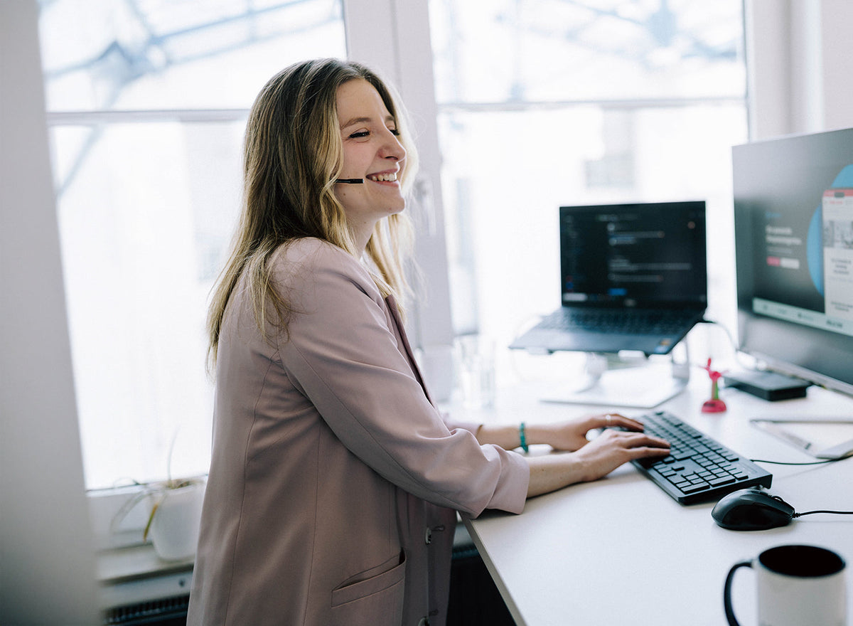 Online Marketing Managerin mit Headset an zwei Monitoren